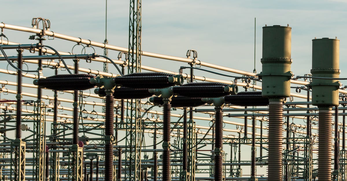 Detailed view of electrical substation with high voltage equipment and insulators against a clear sky.